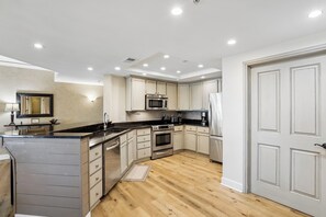 Une cuisine moderne dotée d’appareils électroménagers intégrés, d’un plancher en bois et d’un grand îlot central.