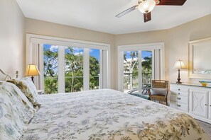 A bedroom with a large bed, a ceiling fan, a balcony with a chair, and a view of greenery. - Ocean Front 4Br Villa w/ Large Balcony! (Hilton Head Island)
