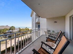 A balcony with a view of the beach, a table with chairs, and a railing.