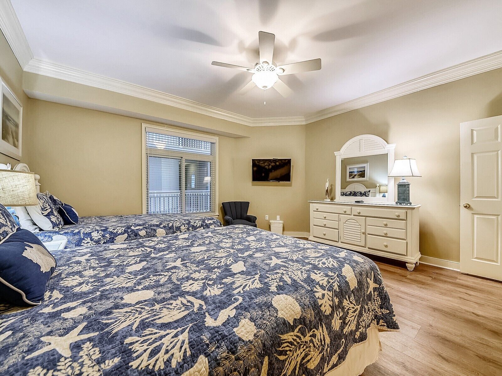 A bedroom with a bed, a dresser, a chair, a ceiling fan, a window, and a door.