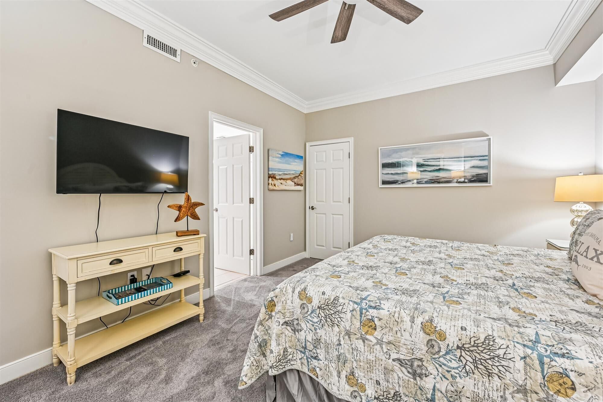 A bedroom with a large bed, a TV mounted on the wall, a dresser, and a ceiling fan.