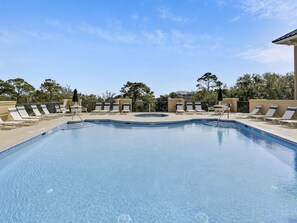 Ein Pool mit Liegestühlen und einem Whirlpool, umgeben von Bäumen und wolkenlosem Himmel.