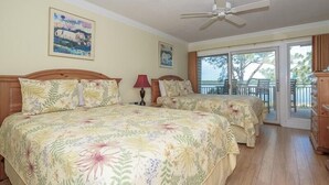Un dormitorio con dos camas, ventilador de techo y balcón con vistas.