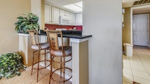 A kitchen with white cabinets, a black countertop, and a microwave. There are two bamboo chairs with cushioned seats. A potted plant is on the floor next to the chairs. - Upscale Villa w/ Panoramic Views of the Sound! (Hilton Head Island)