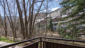 Una scala in legno conduce a un balcone con vista su una zona boschiva, sullo sfondo si scorge un edificio.