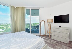 Una camera d'hotel con un letto, televisione, un comò e un balcone con vista sulla città.