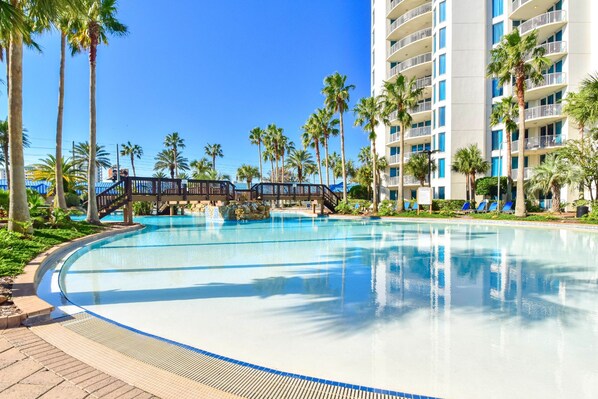 A large swimming pool surrounded by palm trees and a multi-story hotel building.