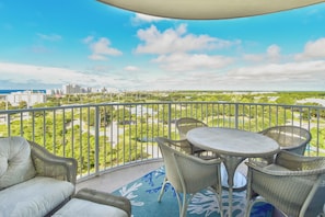 A balcony with wicker furniture, a view of a cityscape, and a clear sky.