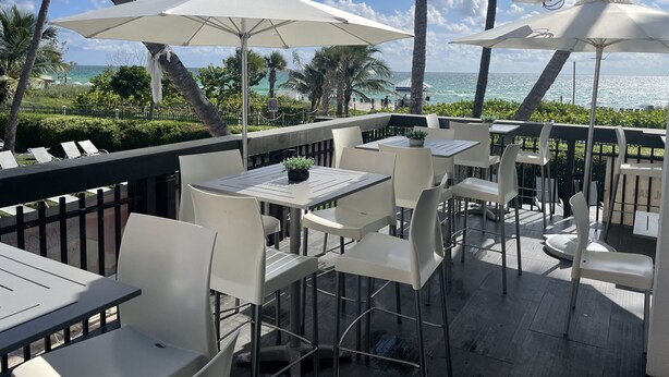 An outdoor seating area with white tables and chairs, umbrellas, and a view of the ocean. - The Alexander Resort Ocean Front (Miami Beach)