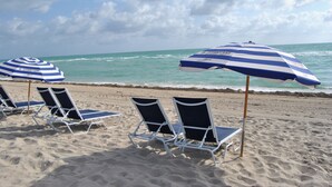 A beach with three lounge chairs and two striped beach umbrellas. - The Alexander Resort Ocean Front (Miami Beach)