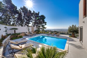 A swimming pool with lounge chairs, surrounded by greenery and a view of the landscape. - Luxury Villa Seventh Heaven with heated pool, hot tub, gym, panoramic views (Klis)