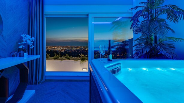 A modern bathroom with a large bathtub, a view of a cityscape, and a potted palm tree. - Luxury Villa Seventh Heaven with heated pool, hot tub, gym, panoramic views (Klis)