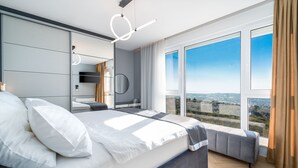 A modern bedroom with a large bed, a bedside table, a mirror, and a view of the city through large windows. - Luxury Villa Seventh Heaven with heated pool, hot tub, gym, panoramic views (Klis)