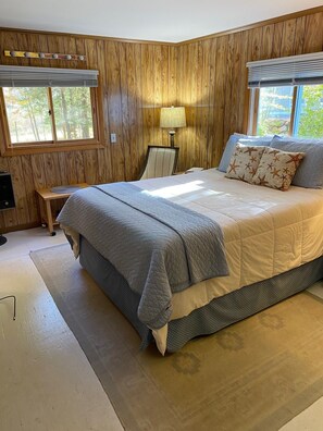 A bedroom with a large bed, wooden panel walls, a desk, and a chair.