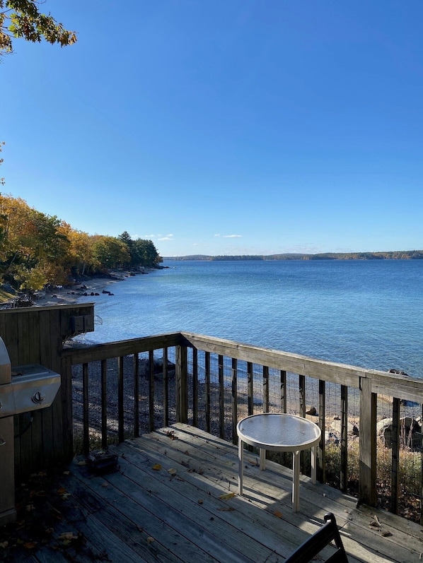A wooden deck with a grill and a table overlooking a calm body of water.