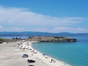 En strand med en lang sandstrand, nogle parkerede biler og få mennesker.