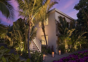 Uma casa moderna com escada, rodeada por plantas tropicais e iluminada por iluminação ambiente.