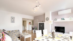 A modern living room with a sofa, dining table, and TV. There is a bookshelf, a plant, and a vase with flowers. - MARCOS. Beautiful apartment in Puerto Pollensa (Puerto Pollensa)