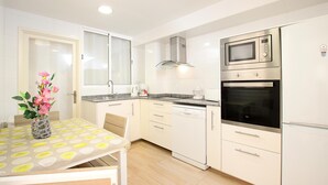 A modern kitchen with white cabinets, a stainless steel microwave, oven, and dishwasher. There is a dining table with a vase of flowers. - MARCOS. Beautiful apartment in Puerto Pollensa (Puerto Pollensa)