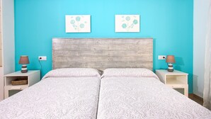 A double bed with a white quilted bedspread, two bedside tables with lamps, and two wall-mounted floral artwork. - MARCOS. Beautiful apartment in Puerto Pollensa (Puerto Pollensa)
