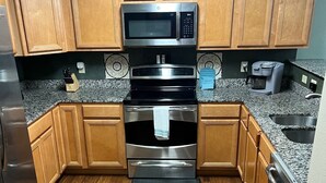 Una cocina con armarios de madera, microondas de acero inoxidable, horno y lavavajillas.