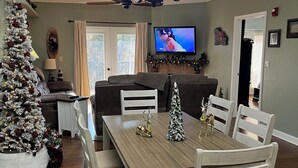 Comedor con una mesa de madera y sillas blancas, una araña y un árbol de Navidad.