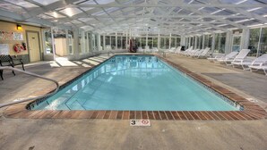 Una piscina interior con techo de cristal, tumbonas y puesto de socorrista.