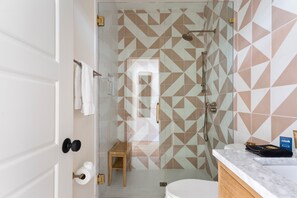A modern bathroom with a geometric tile backsplash, a glass shower enclosure, a wooden bench, and a marble countertop. - Only 2 Blocks to King! | The Blue Note (Charleston)