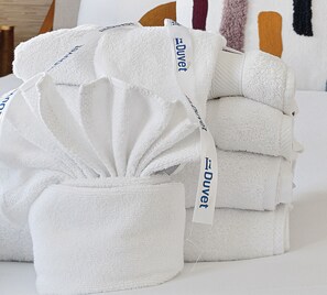 A stack of white towels with 'Duvet' tags, neatly arranged on a bed. - Only 2 Blocks to King! | The Blue Note (Charleston)