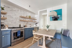 A modern kitchen with blue cabinets, a wooden dining table, and a hanging light fixture.