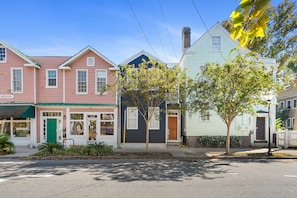 Une rangée de maisons de ville aux couleurs vives, avec une porte verte, une pancarte indiquant « à louer » et un arbre devant.