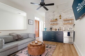 A modern living room with a grey sofa, a brown ottoman, and a ceiling fan.