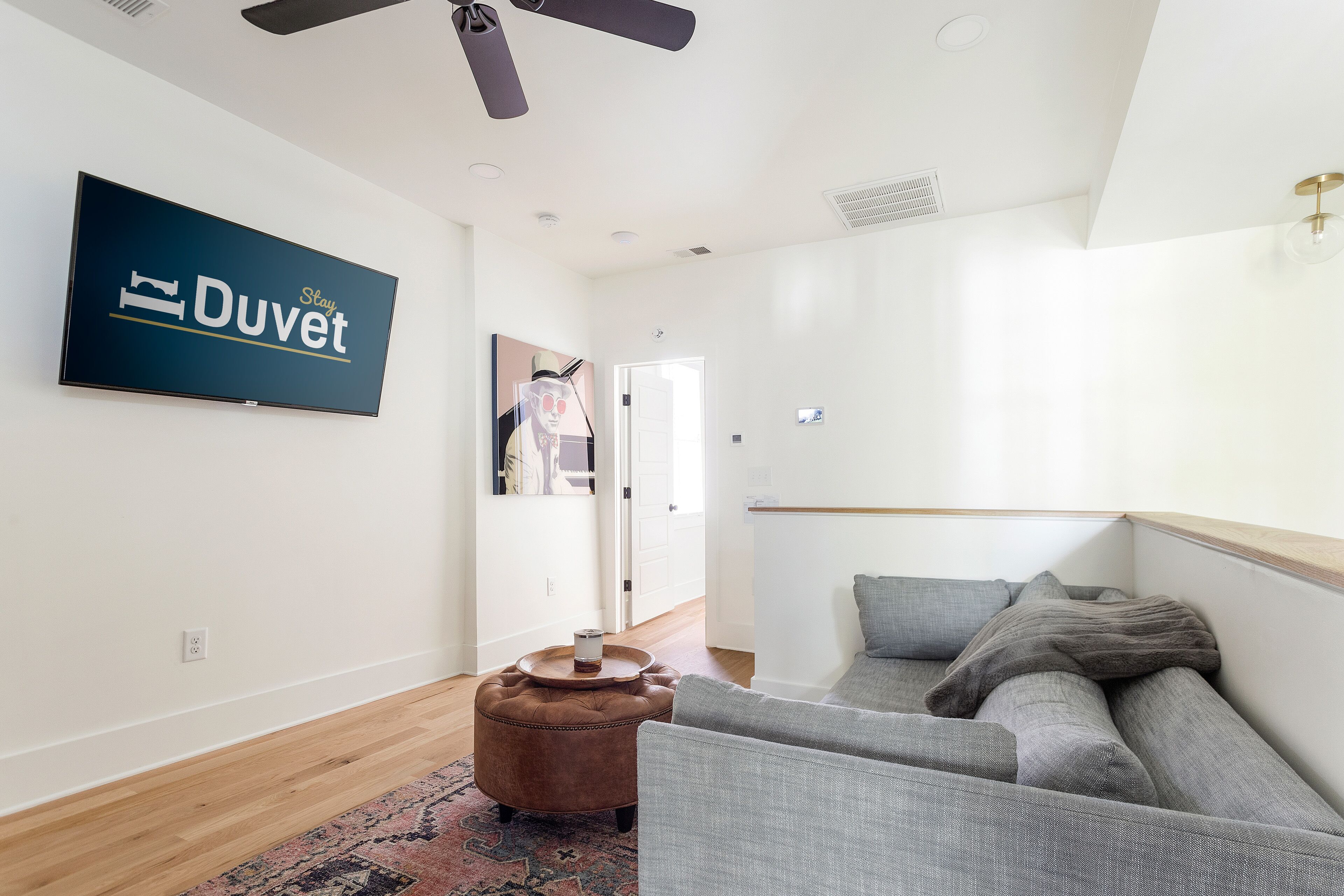 Un salon moderne avec un téléviseur à écran plat, un pouf marron et un canapé gris.
