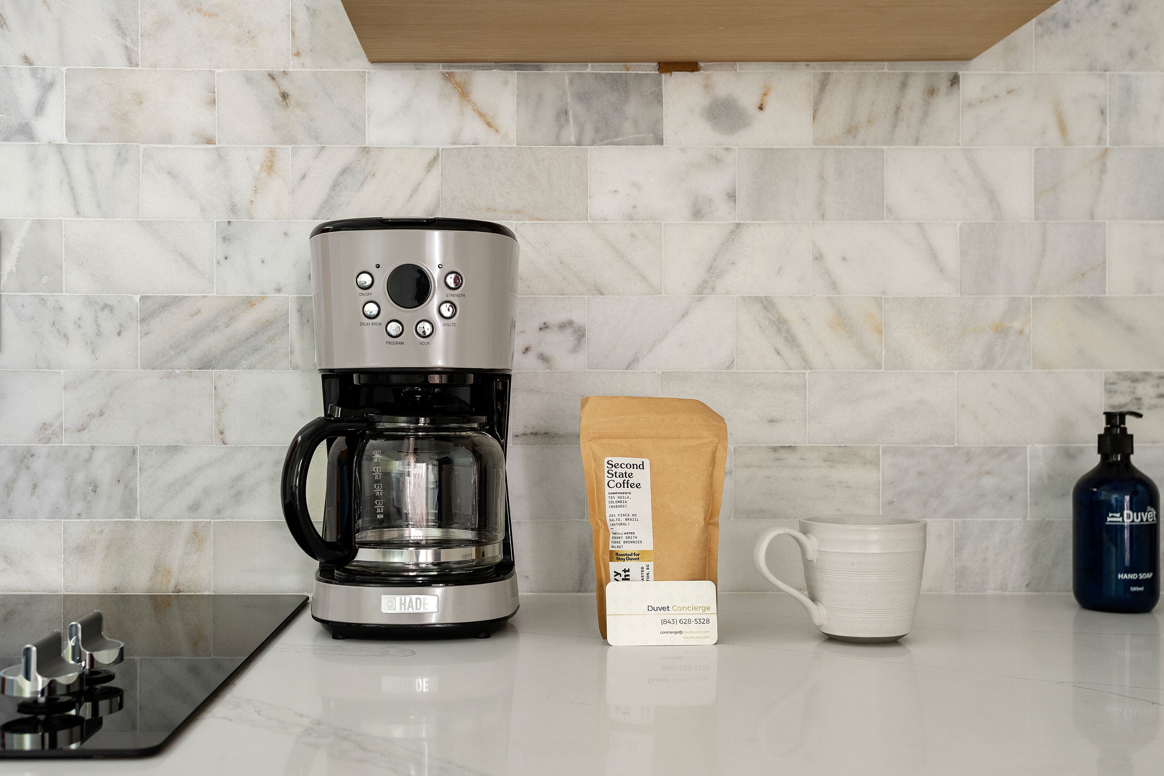 A coffee maker, a coffee bag, a mug, and a hand soap bottle on a kitchen counter.
