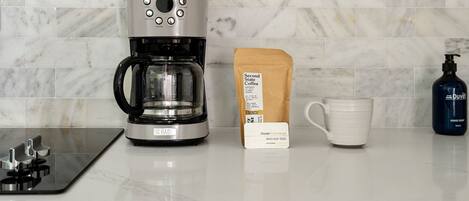 A coffee maker, a coffee bag, a mug, and a hand soap bottle on a kitchen counter.