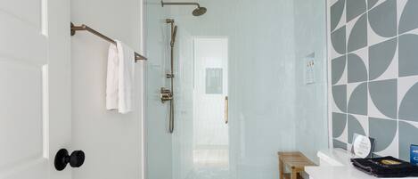A modern bathroom with a glass-enclosed shower, a white toilet, and a small wooden stool.