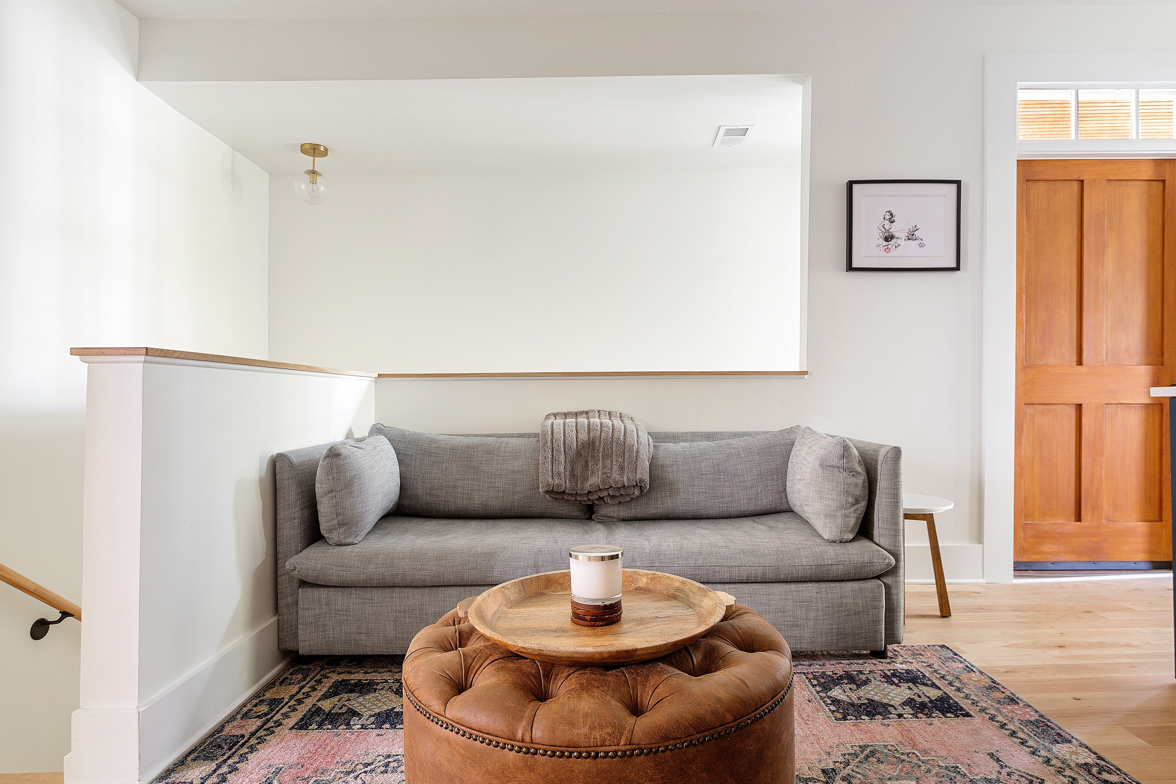 Un salon avec un canapé gris, un pouf rond, une petite table et un tableau encadré au mur.