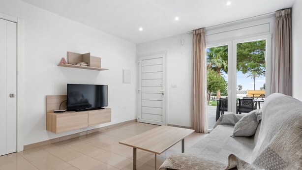 A modern living room with a flat-screen TV on a wooden console, a beige sofa, and a glass door leading to an outdoor area.