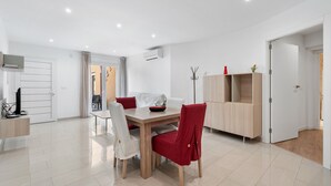 A modern dining area with a wooden table and red chairs, a white chair, and a cabinet with shelves.