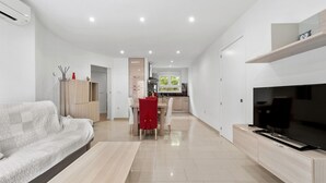 A modern living room with a sofa, a coffee table, a TV, and a dining area with a red tablecloth.