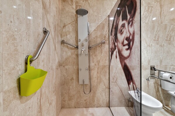 Un baño moderno con ducha, barra de apoyo y un cubo amarillo.