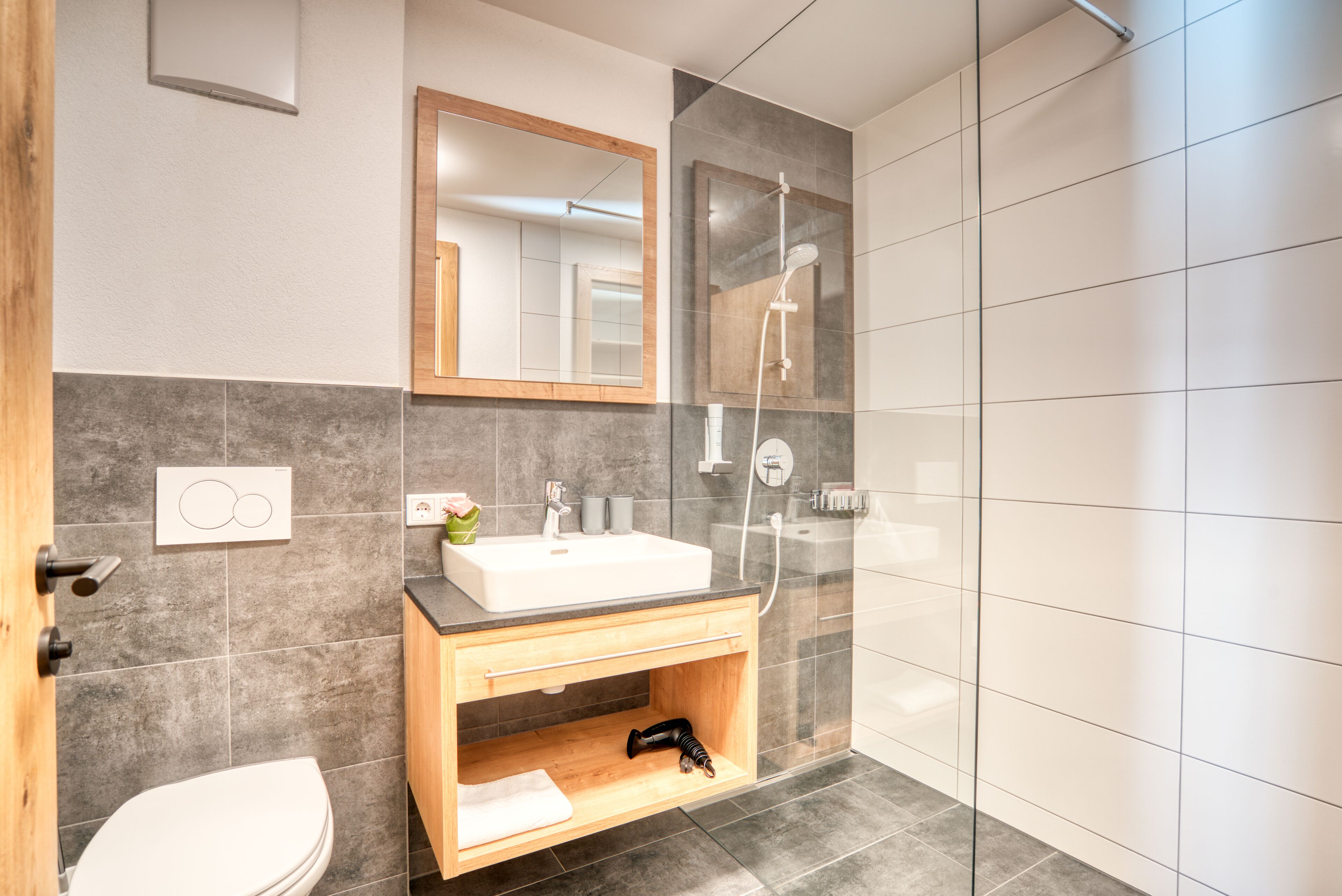 Ein modernes Badezimmer mit einem Holzkosmetikschrank, einem weißen Waschbecken, einem Spiegel, einer Dusche und einem WC.