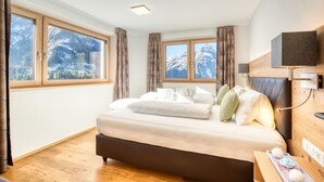 A bedroom with a bed, wooden floor, curtains, a TV, and a window with a mountain view. - HUS 23 (Schroecken)