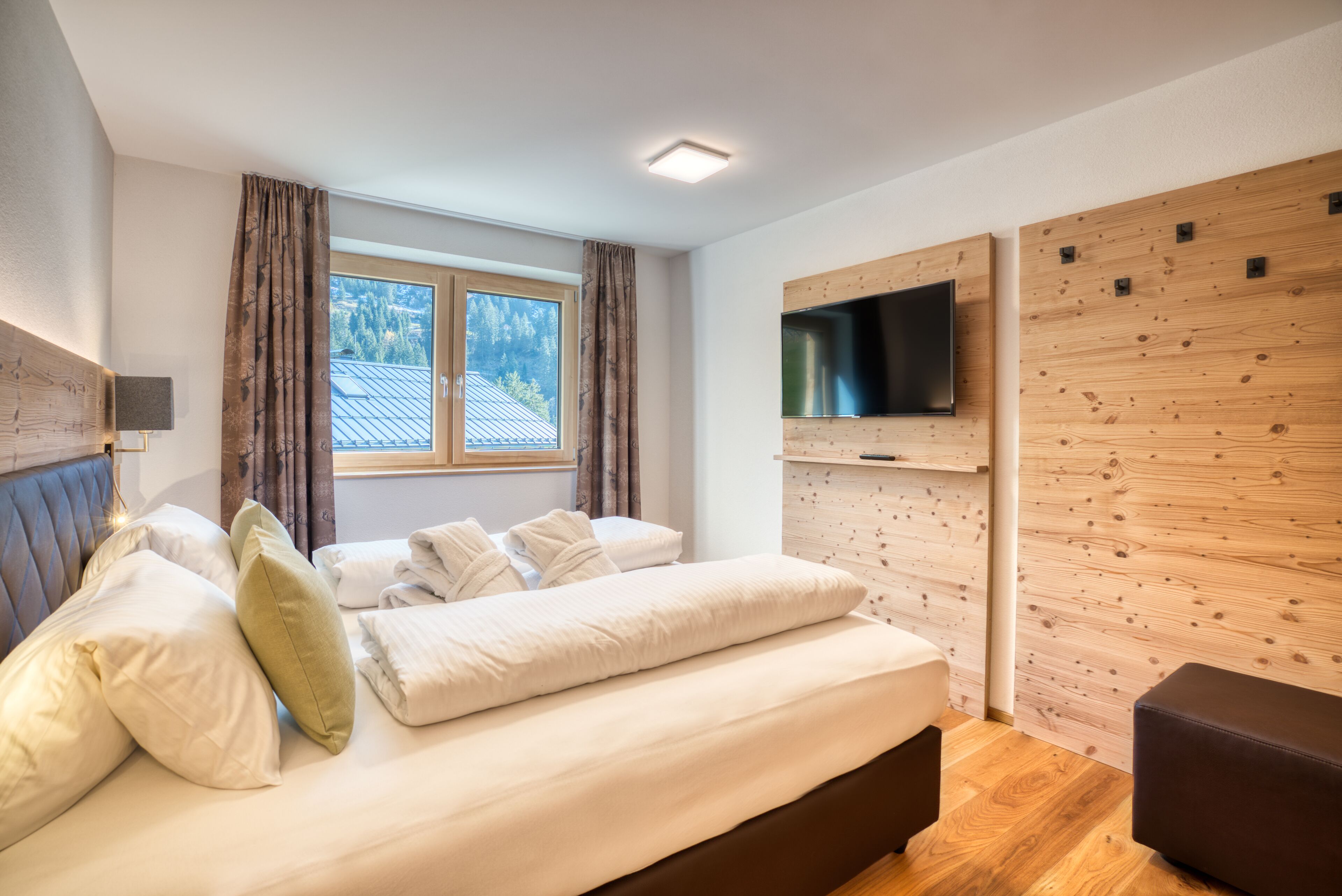 Une chambre moderne avec un lit, un téléviseur fixé au mur en bois et une fenêtre avec des rideaux.