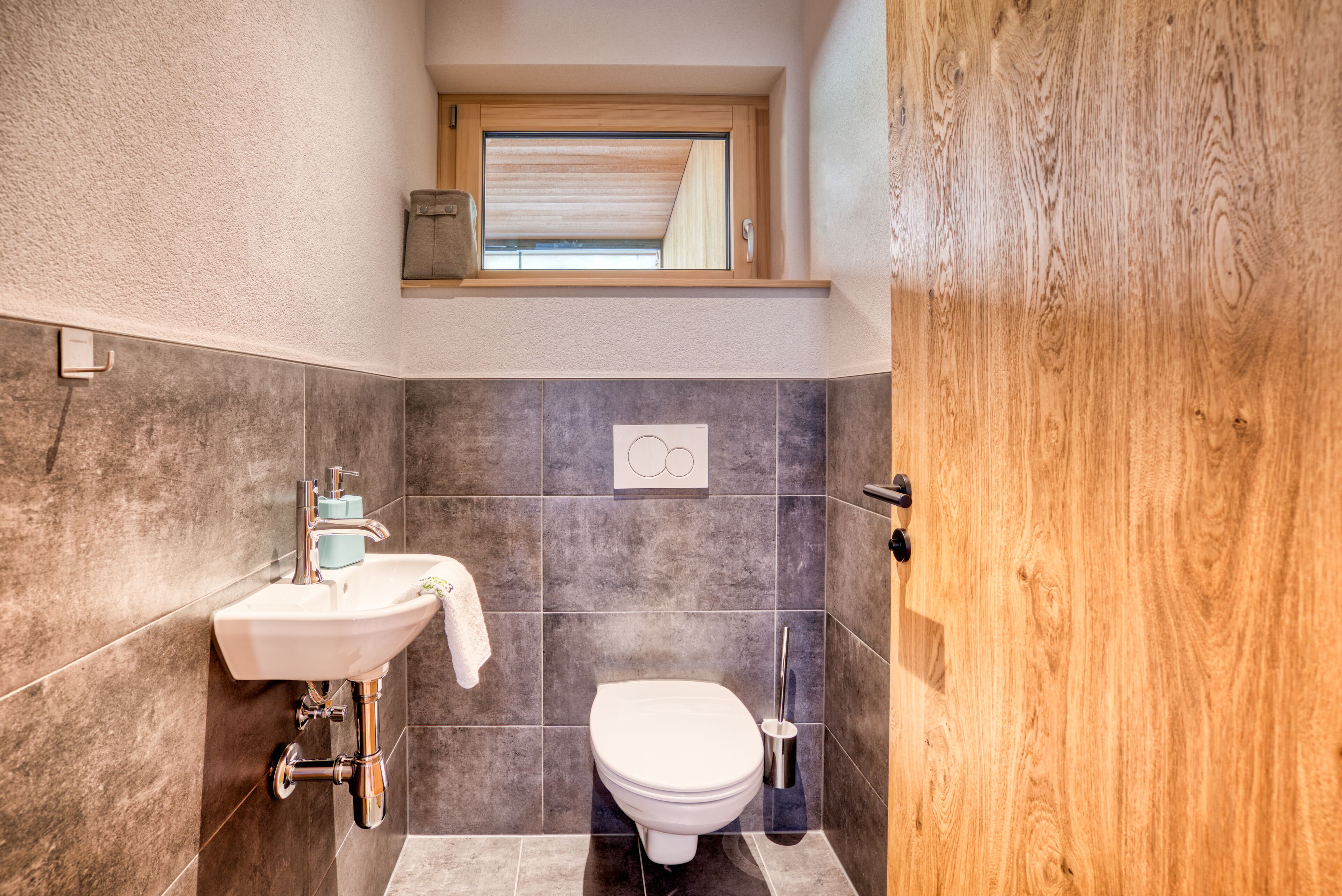 Un baño moderno con lavamanos, inodoro y ventana sobre el inodoro.