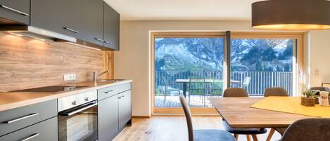 A modern kitchen with a large window, wooden flooring, and a dining area with a table and chairs.