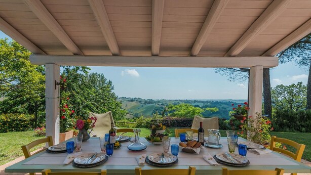 Un espace extérieur abrité, aménagé pour les repas, avec une table dressée pour quatre personnes, entourée de chaises, et offrant une vue sur un paysage pittoresque.