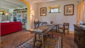 Un salon chaleureux avec un canapé rouge, une table à manger en bois entourée de chaises, une bibliothèque et un tapis à motifs.