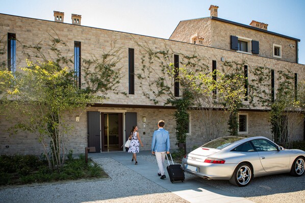 A building with a stone facade, a car parked in front, and a person with a suitcase walking towards the entrance.