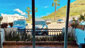 A balcony with a view of parked cars and palm trees, wooden flooring, and potted plants. - COMFORTABLE APARTMENT WITH POOL, WHIRLPOOL BATHTUB, 70" TV AND MORE (Cabo San Lucas)